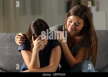 Bad hypocrite friend comforting a sad girl sitting on a couch in the living room at home Stock Photo