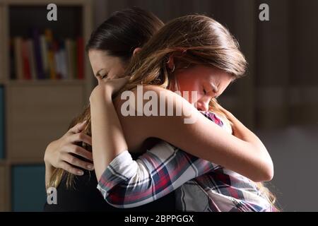 Side view of two sad good friends embracing in a bedroom in a house interior with a dark light in the background Stock Photo