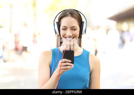 Front view portrait of a girl listening to music on a phone wearing headphones on the street Stock Photo