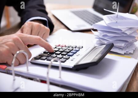 Close-up Of Businessman's Hand Using Calculator While Calculating Invoice On Desk Stock Photo