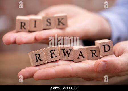 Close-up Businessman's Hand Holding Risk And Rewards Blocks Over Wooden Table Stock Photo