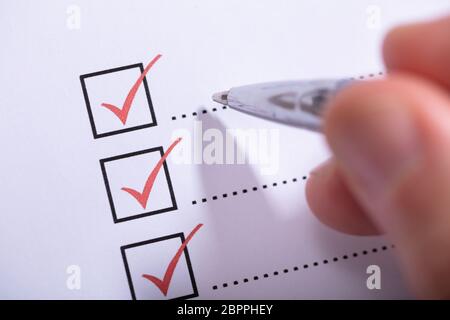 Close-up Of Person's Hand Marking On Checklist With Pen Stock Photo