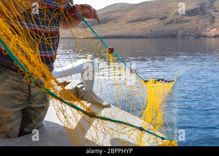 Fisherman is fishing fresh fishes using yellow fishing nets, on fishing boat, Crete, Greece. Stock Photo