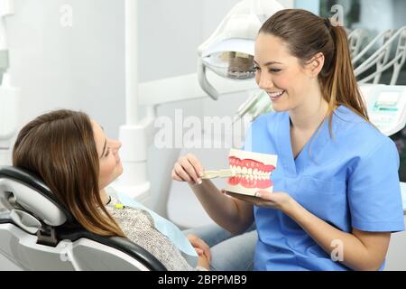 Dentist explaining how to brush teeth correctly to a patient after treatments sitting on a chair in a clinic box with medical equipment in the backgro Stock Photo