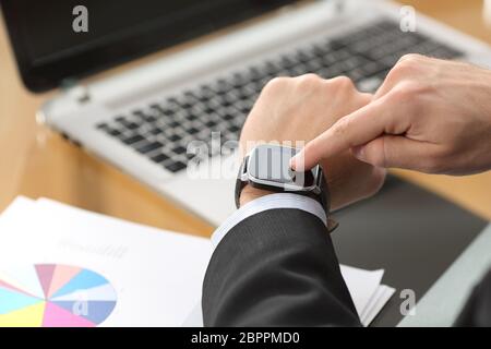 Businessman hands using a smart watch with the finger on the touch screen sitting in a desktop at office with a computer in the background Stock Photo