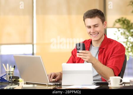 Happy businessman working online with multiple devices and holding a smart phone in a desk at office Stock Photo