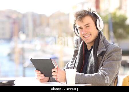 Portrait of a happy man e-learning looking at camera in a coffee shop in winter Stock Photo