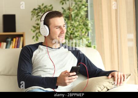 Handsome guy listening music and relaxing sitting on a sofa and looking through the window of the living room at home Stock Photo