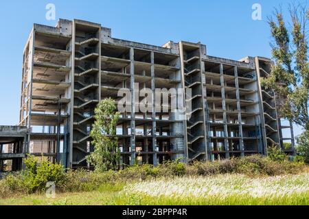 Huge multi floors concrete structure of abandoned building with stairs surrounded by grass and trees with blue sky in the background. Architecture det Stock Photo