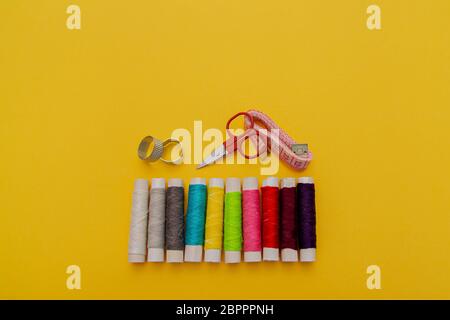 Thread, needles, scissors and meter on yellow background. tailoring set. sewing kit multi-colored Stock Photo