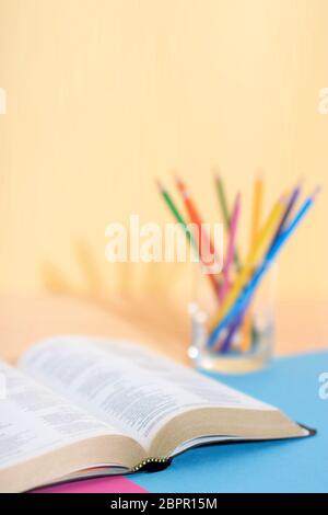 Bible book (blured text) and glass with a set of colored pencils on a colored paper background ready to be studied and underlined. Ready for Bible stu Stock Photo