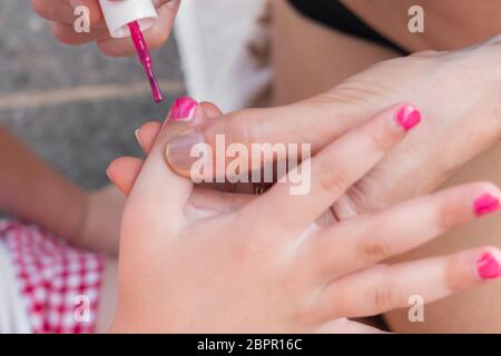 Woman applying nail polish, doing manicure to a little girl, fun activity at home, girl birthday party, spring and summertime. Stock Photo