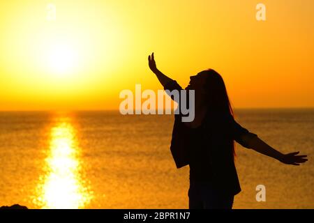 Silhouette of an excirted girl stretching arms at sunset celebrating success on the beach