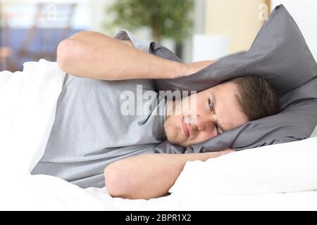 One man trying to sleep covering ears to avoid neighbor noise at home or hotel Stock Photo