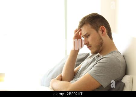Sad single man lamenting sitting on the bed on the bed of an hotel room or home Stock Photo