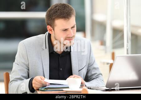 Executive comparing documents on line with a laptop sitting in a coffee shop Stock Photo