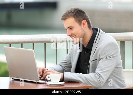 Happy executive writing in a laptop sitting in a bar outdoors Stock Photo
