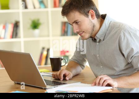 Serious freelancer working checking on line content in a laptop on a desk at home Stock Photo