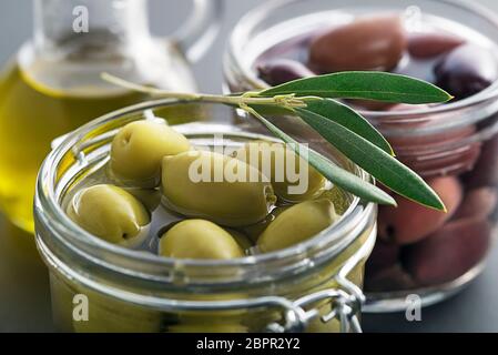 Pickled green and black olives in glass jar with branch leaves close up Stock Photo