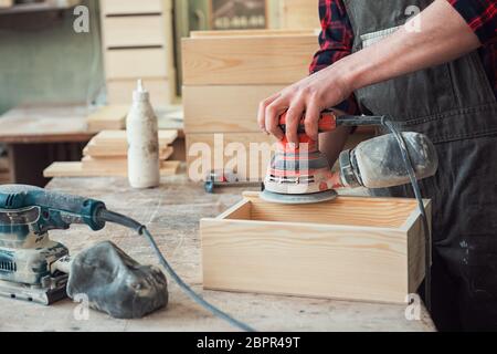 Worker grinds the wood box of angular grinding machine Stock Photo