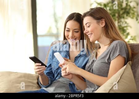 Two roommates using their smart phones on line at home sitting on a sofa in the living room at home Stock Photo