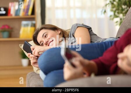 Two happy roommates using their smart phones lying on a couch at home Stock Photo