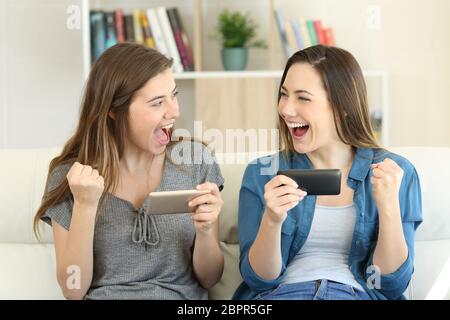 Excited friends playing online game and winning sitting on a couch in the living room at home Stock Photo