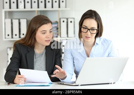 Two concentrated office workers comparing paper documents on-line with a laptop Stock Photo