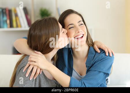 Happy girl kissing her friend sitting on a couch in the living room at home Stock Photo