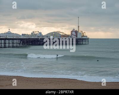 Surfers braving December cold sea by Brighton Pier on overcast winter day. Stock Photo