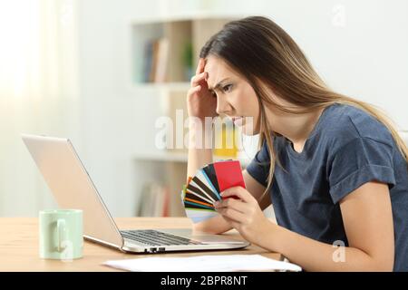 Side view portrait of a worried shopper holding multiple credit cards checking online purchases Stock Photo