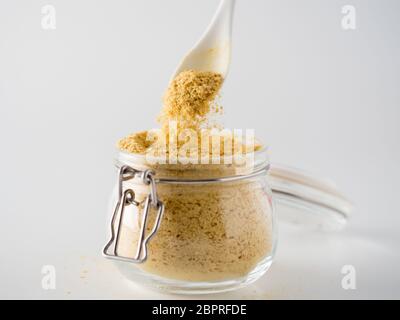 Nutritional yeast background. Nutritional inactive yeast falling from spoon in glass jar on white background. Copy space. Nutritional yeast is vegetar Stock Photo