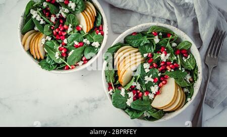 Fresh salad with baby spinach, pear, pomegranate and cottage cheese. Two bowls with delicious summer fruit salad on marble table. Copy space for text. Stock Photo