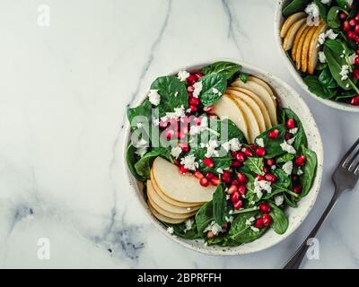 Fresh salad with baby spinach, pear, pomegranate and cottage cheese. Two bowls with delicious summer fruit salad on marble table. Copy space for text. Stock Photo