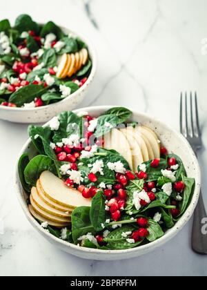 Fresh salad with baby spinach, pear, pomegranate and cottage cheese. Two bowls with delicious summer fruit salad on marble table. Copy space for text. Stock Photo