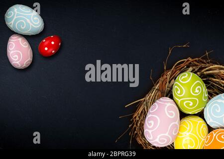 Colorful happy easter eggs in bird nest and tulips on dark empty slate stone blackboard with copy space design pattern Stock Photo