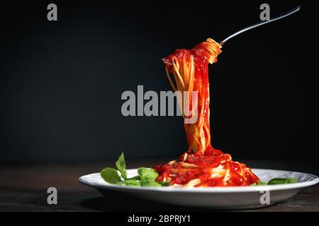 Tasty appetizing classic italian spaghetti pasta with tomato sauce, cheese parmesan and basil on plate on dark table Stock Photo