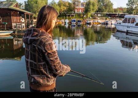 Man with long hair is fishing at river corner from raft. Boats and floating  houses are around him with trees in background. He is using fishing rod wi  Stock Photo - Alamy