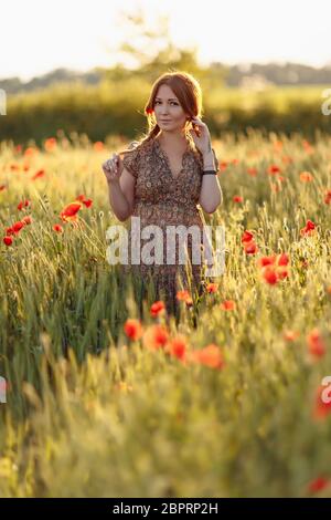 Redhead woman on green field with poppies in summer sunset Stock Photo