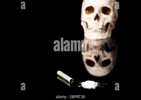 cocaine or other illegal drugs that are sniffed by means of a tube and Skull, isolated on black glossy background Stock Photo