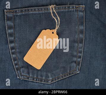 tied on a rope is an empty rectangular brown paper tag on blue jeans, full frame Stock Photo