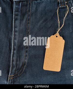 tied on a rope is an empty rectangular brown paper tag on blue jeans, full frame Stock Photo