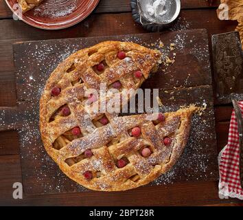 round apple pie on a rectangular old brown cutting board sprinkled with powdered sugar, top view Stock Photo