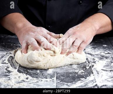 baker kneads white wheat flour dough on a black wooden table Stock Photo