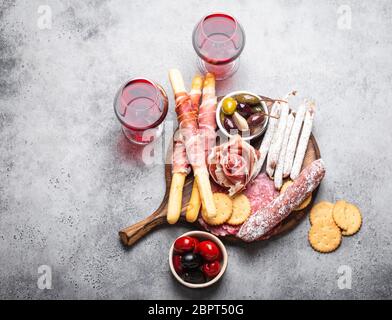 Variety of cold meat cuts and appetizers, red wine, prosciutto, jamon, salami slices, sausage, grissini, olives. Assorted mix of meat on rustic wooden Stock Photo