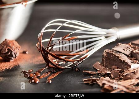 Dripping melted chocolate on an old vintage whisk alongside a round bonbon or cookie and chopped bar of chocolate Stock Photo
