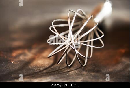 Old vintage steel wire whisk on a rustic wooden kitchen table in a close up view to the end Stock Photo