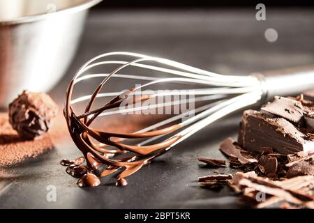 Chocolate coated old vintage metal whisk alongside chopped chocolate and a cacao bonbon on a kitchen table in close up view Stock Photo