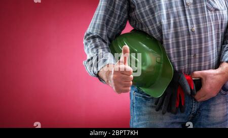 Caucasian construction worker in jeans and shirt, with helmet and protective gloves making ok sign with thumb up. Construction industry. Job security. Stock Photo