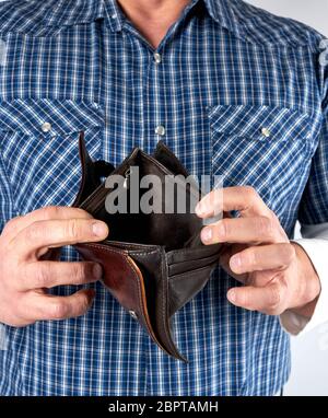 man in blue plaid shirt holds open empty leather wallet, poverty concept Stock Photo